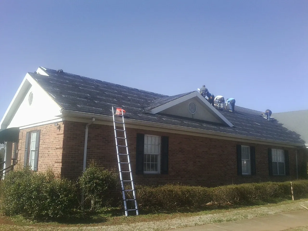 Crew tearing shingles off a brick ranch roof with a ladder set — Metal Roof Repair work by our crew in White Marsh