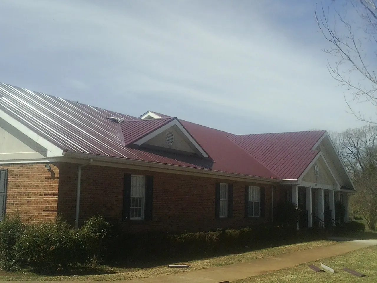 Red metal roof with gabled entries on a long brick building, from a Hail Damage Roof Repair job in White Marsh