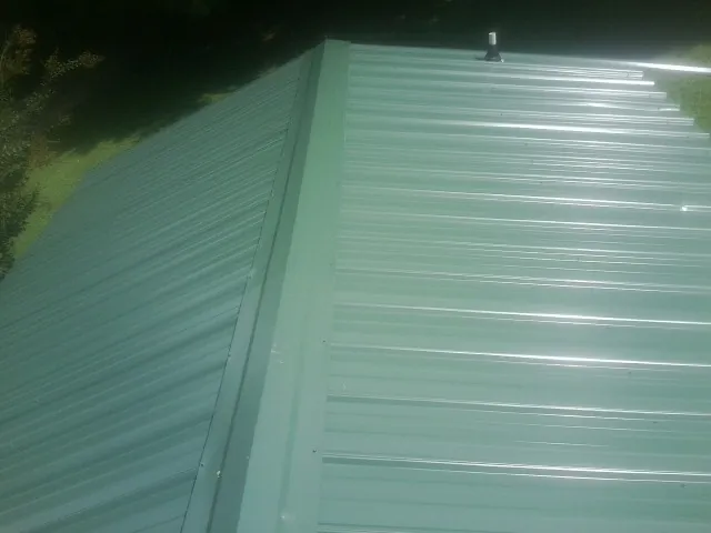 New green metal panels meeting at the ridge of a roof — Flat Roof Repair work by our crew in White Marsh