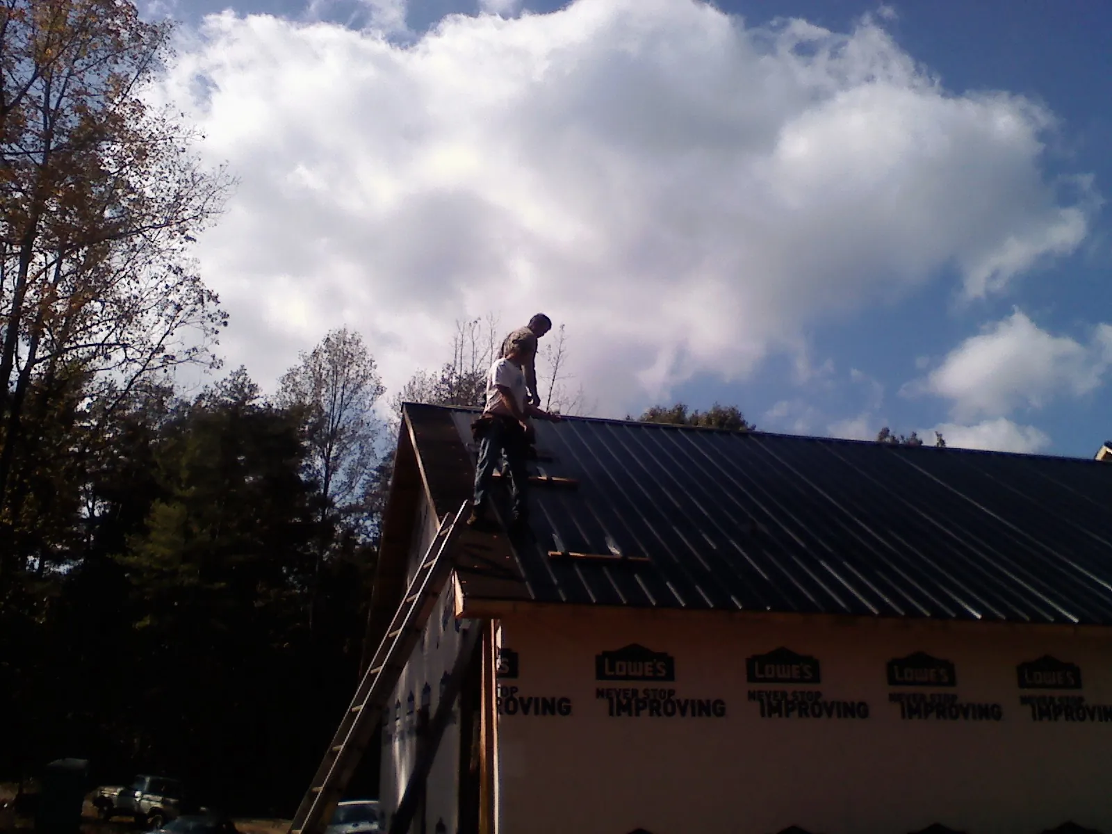 Roofer fastening dark metal panels high against a cloudy sky, from a Roof Inspection job in White Marsh