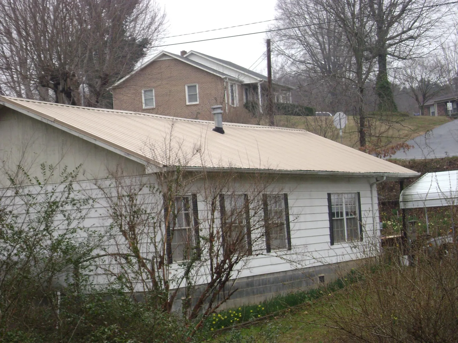 Tan metal roof on a white sided house set into a hillside — Commercial Roofing by Roofing Brothers in White Marsh